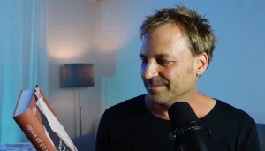 Der Autor Daniel Mezger sitzt vor einem Mikrophon, mit seinem Buch in der Hand