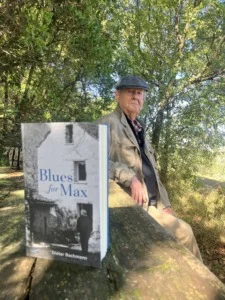 Der Autor Dieter Bachmann sitz im Wald an einem Holztisch, auf dem sein Buch »Blues for Max« steht.